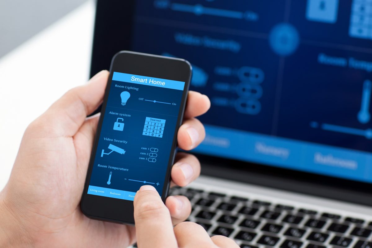 man holding the phone with program smart home on the screen against the background of the computer